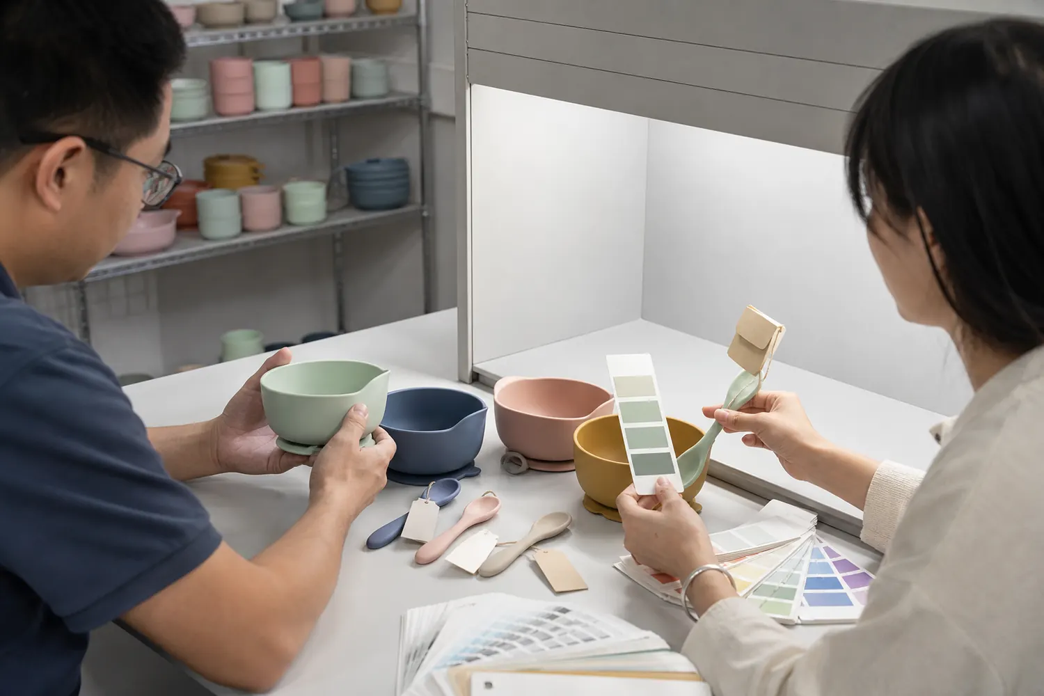 Buyer and silicone color technician comparing molded feeding bowls with physical Pantone color chips under controlled lighting